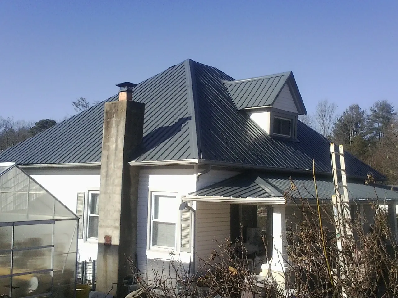 Dark blue standing seam metal roof on a white farmhouse with dormer — Slate & Tile Roof Repair by Roofing Brothers in Mount Summit