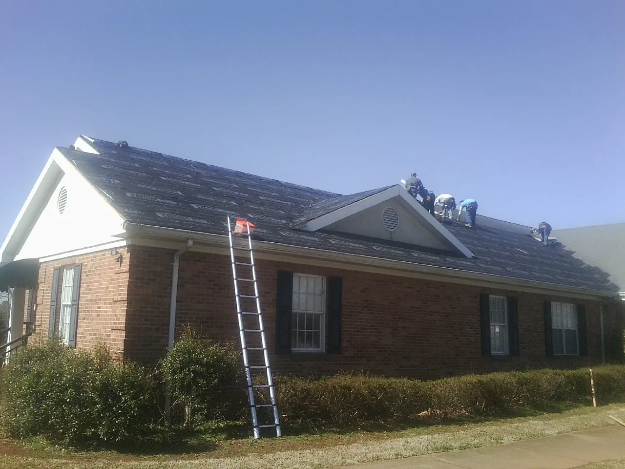 Crew tearing shingles off a brick ranch roof with a ladder set — Emergency Roof Repair work by our crew in Mount Summit