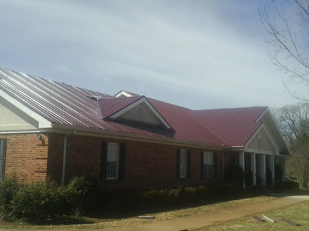 Red metal roof with gabled entries on a long brick building, from a Hail Damage Roof Repair job in Mount Summit