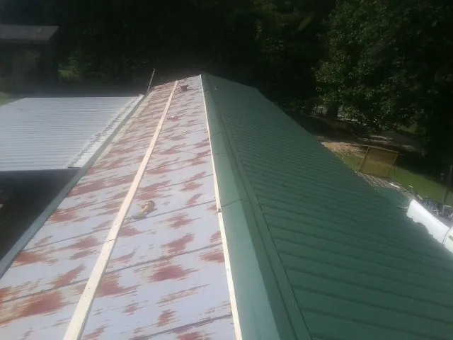 Old rusted panels beside newly installed green metal roofing — Wind Damage Roof Repair by Roofing Brothers in Mount Summit
