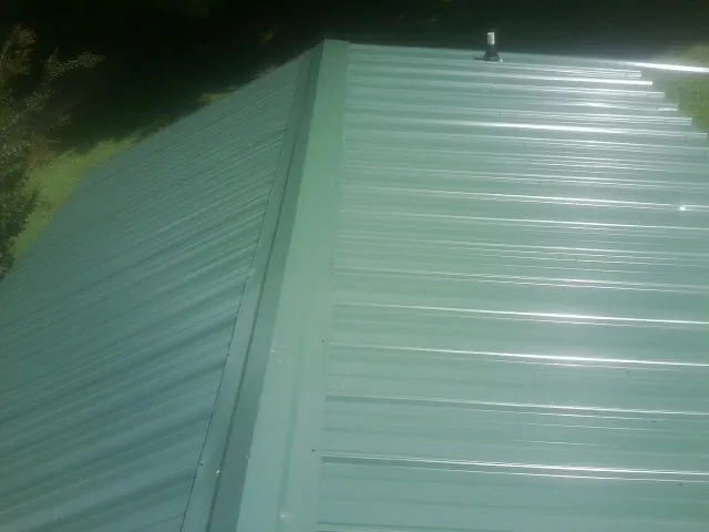 New green metal panels meeting at the ridge of a roof — Flat Roof Repair work by our crew in Mount Summit