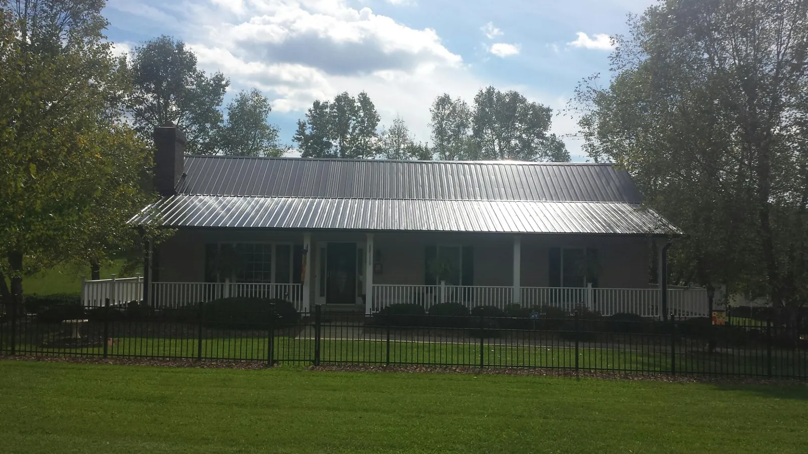 Gray metal roof on a brick ranch with a full width front porch — Gutter Guard Installation work by our crew in Mount Summit