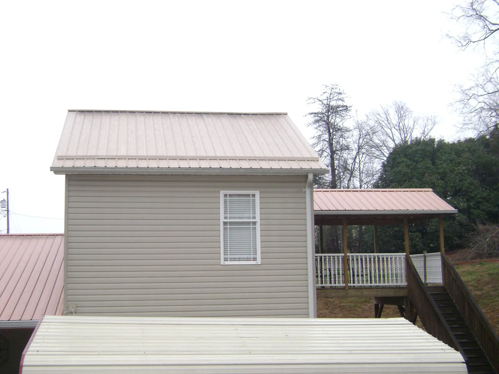 Tan metal roofs on a two story addition and attached porch, from a Roof Replacement job in Mount Summit
